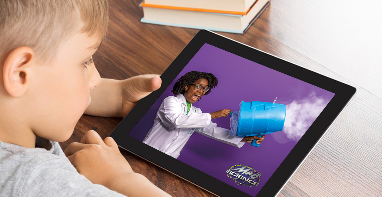 Boy looking at ipad with a mad scientist on the screen blowing smoke out of a smoke machine